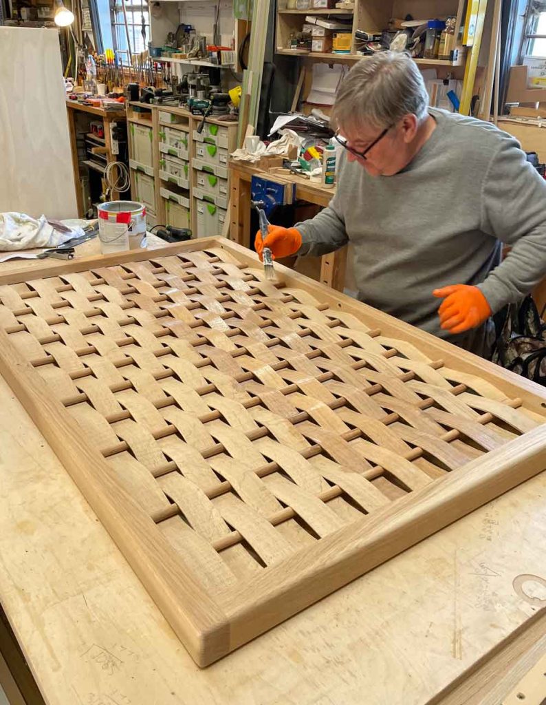 One of our craftsman applying finish to a wooden woven panel in a workshop setting.