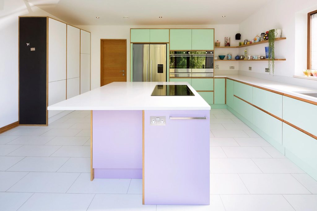 Contemporary plywood kitchen featuring white, mint green and lavender cabinetry with a white countertop and built-in appliances.