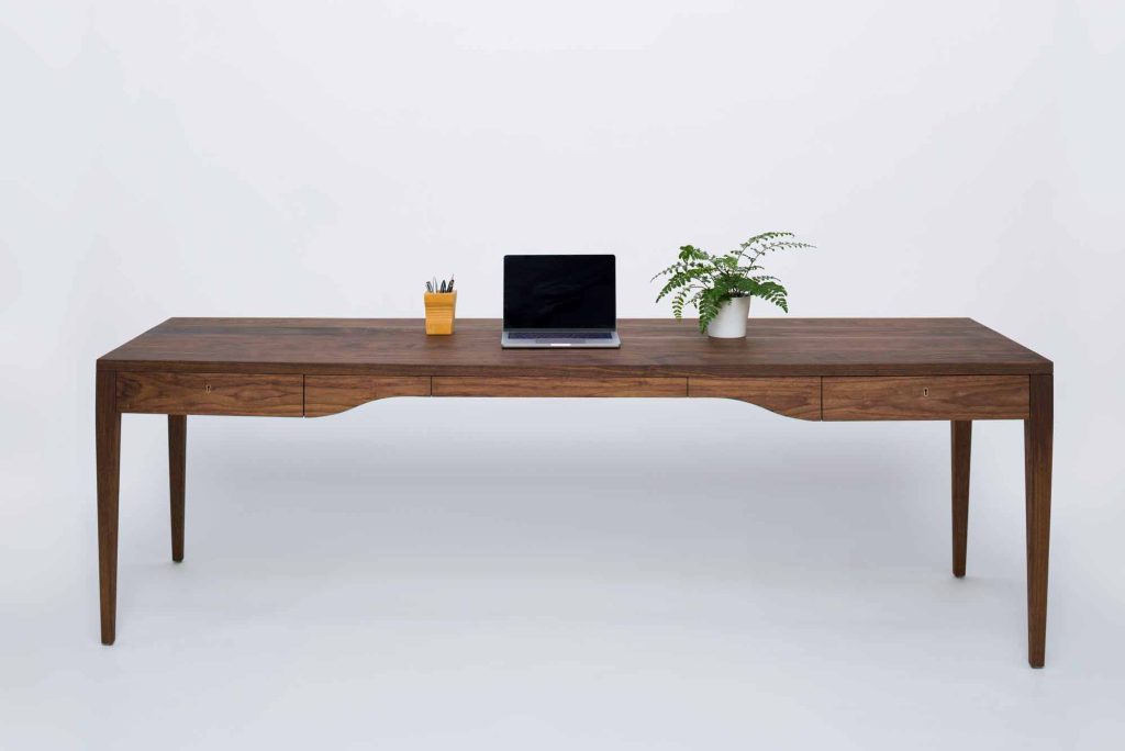 A contemprorary walnut writing desk featuring a laptop, a potted plant, and a pencil holder on top.