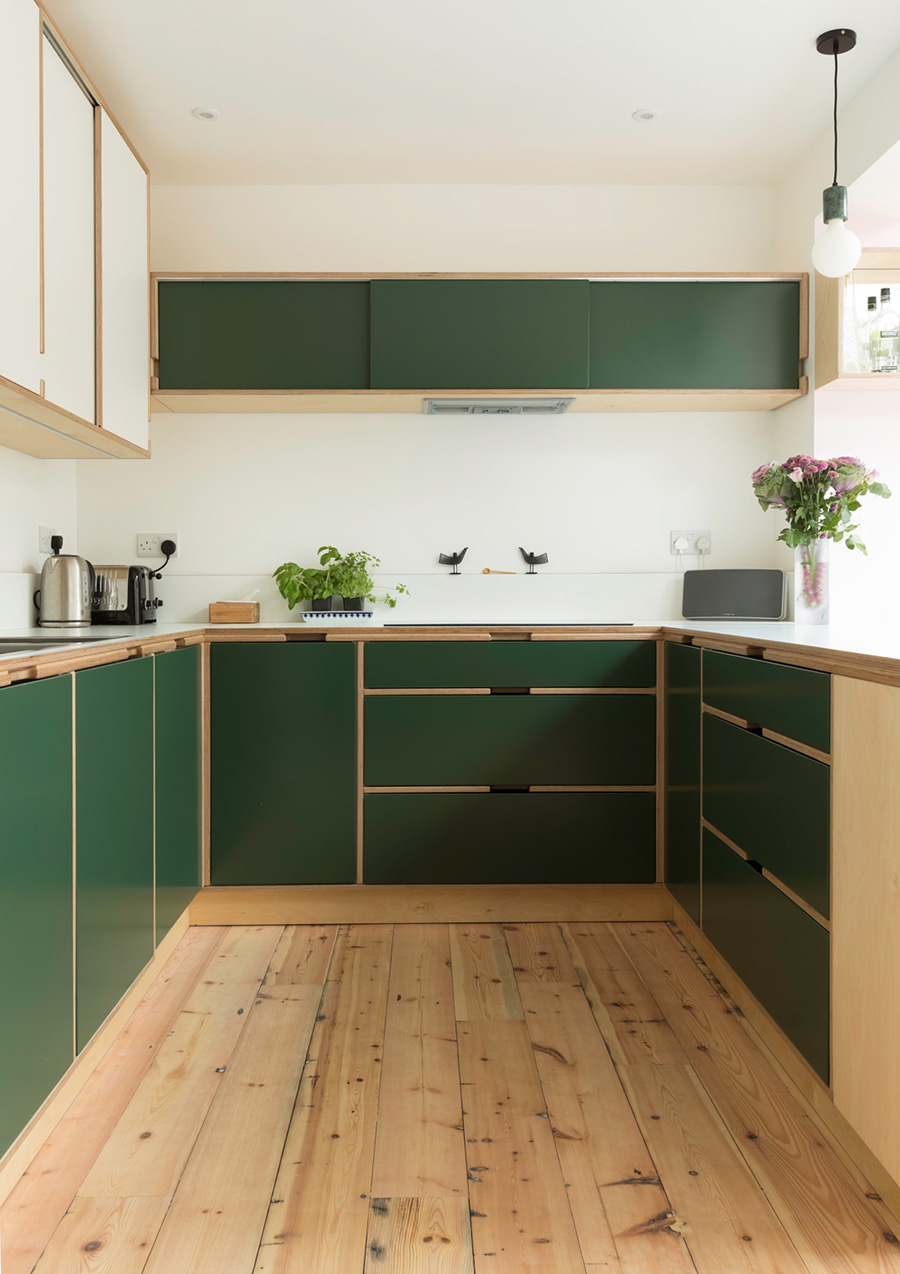 Kitchen dining room with bespoke kitchen which has open shelves for books and a bar and cabinets. The fitted kitchen is made from birch plywood with a combination of white laminate, green lacquer doors and natural birch featuring handleless cut outs within the exposed plywood edge framework.